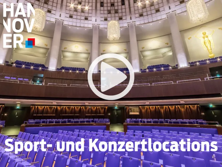 Moderner Konzertsaal in Hannover mit blauen Sitzreihen, hohen Säulen, Kronleuchtern und goldenen Verzierungen.